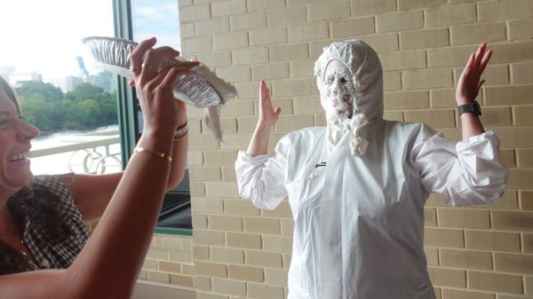 A woman throws a whipped cream pie into a colleague's face