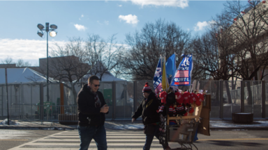 A man and a Trump merchandise vendor cross the street in front of a security checkpoint in front of John Marshall Park during inauguration on Jan 20